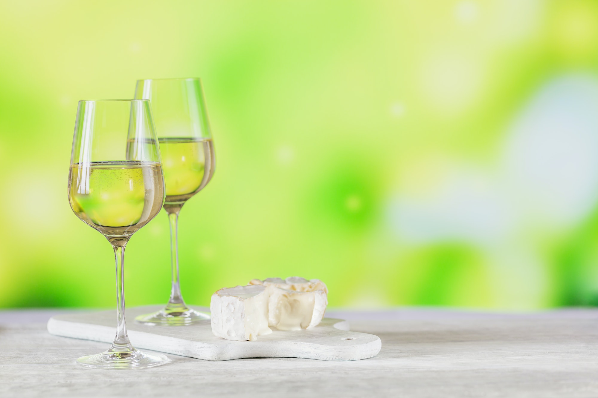 White wine served with cheese plate on light green background.